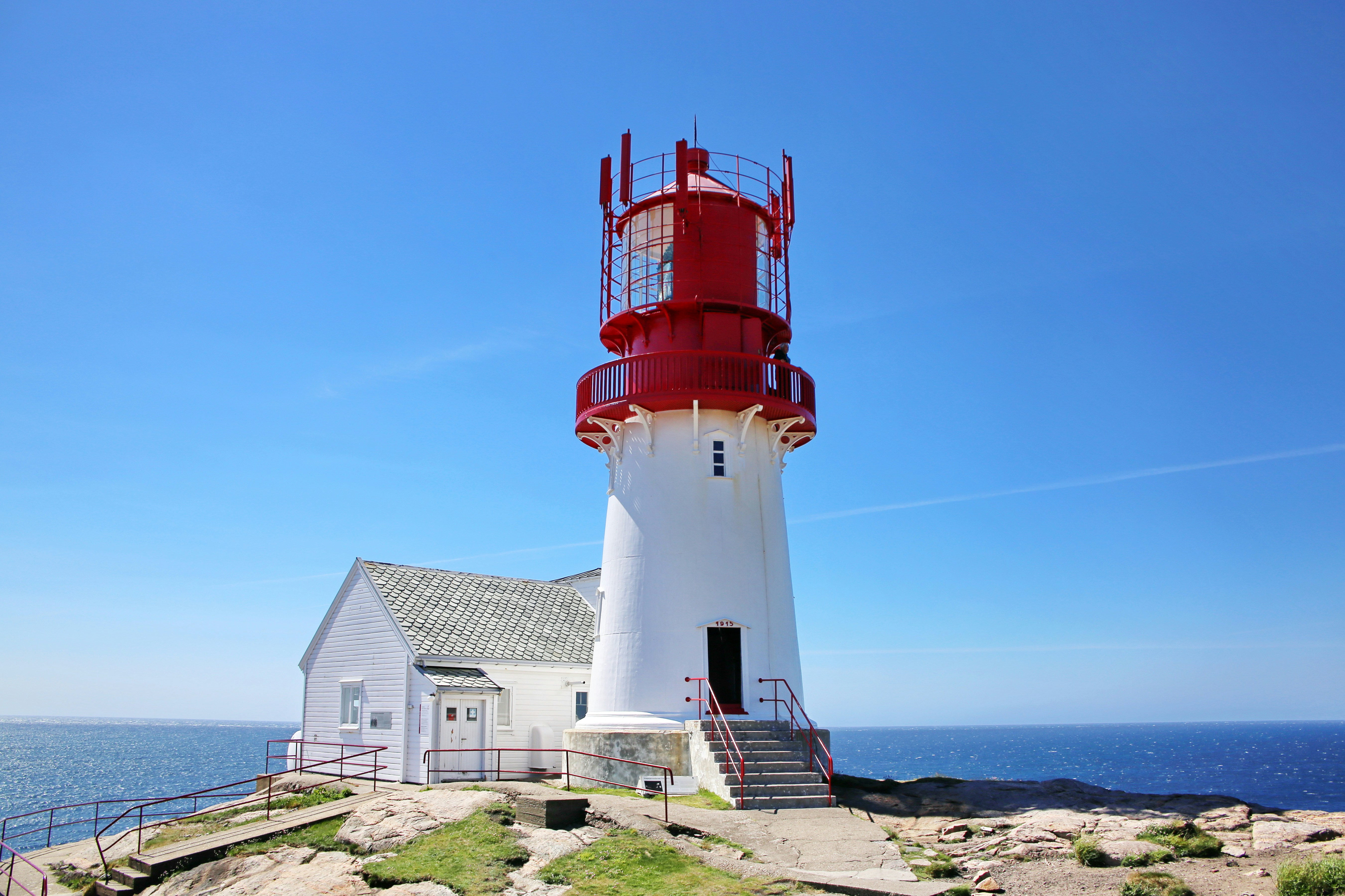 Lindesnes fyr med hvitt tårn og rødt lanternehus mot blå himmel